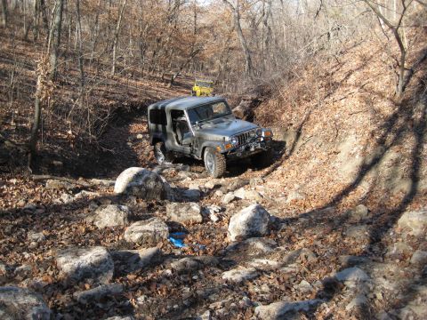 2005 Jeep Wrangler - A gray Jeep Wrangler tackles a challenging off-road course with another Jeep visible further up the trail.