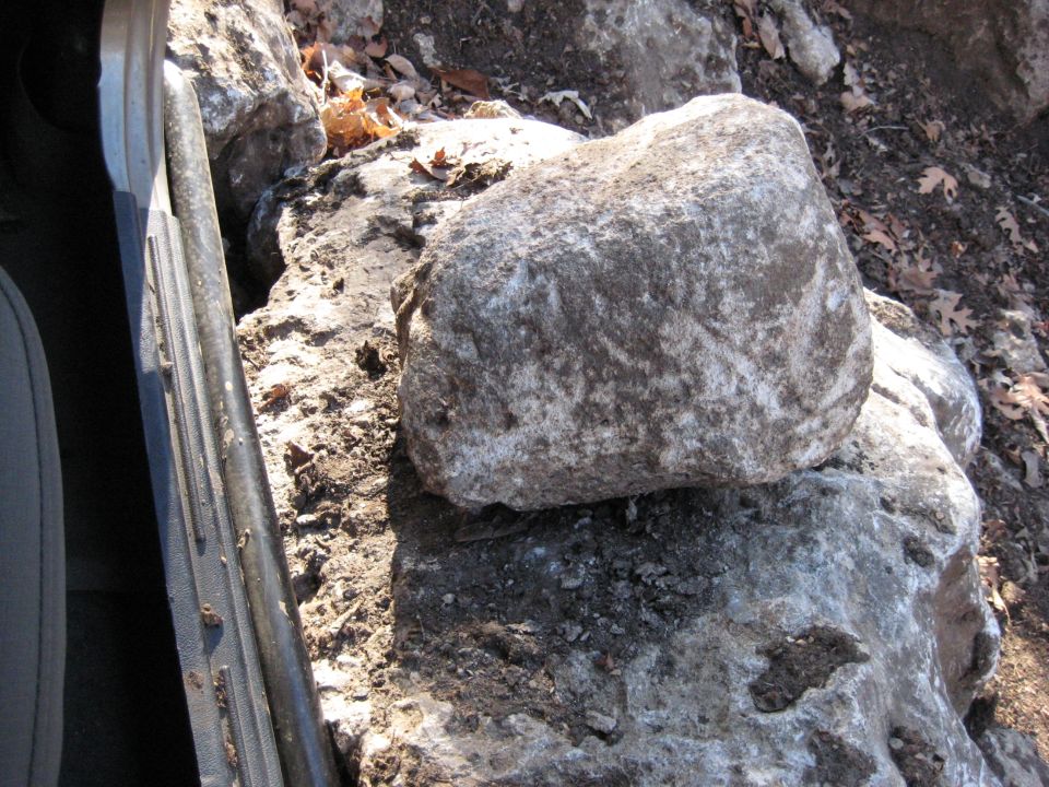 Rock resting on the door sill of a vehicle, with more rocks and dirt in the background