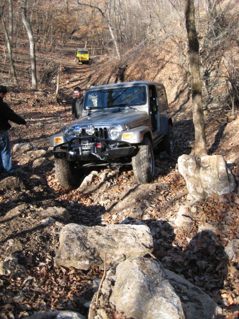 2005 Jeep Wrangler - Two Jeeps tackle a challenging, wooded off-road course during daylight hours.
