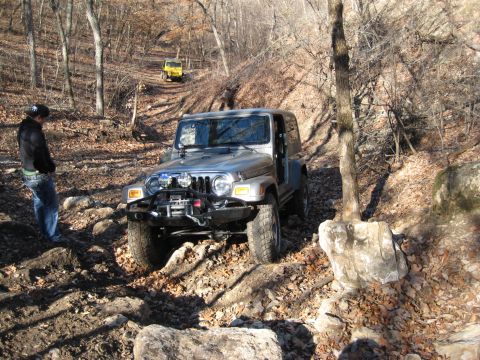 2005 Jeep Wrangler - Two Jeeps navigate a wooded, rocky trail on a sunny day.