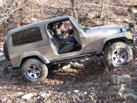 2005 Jeep Wrangler - A driver navigates a brown Jeep Wrangler over a rough, outdoor terrain.