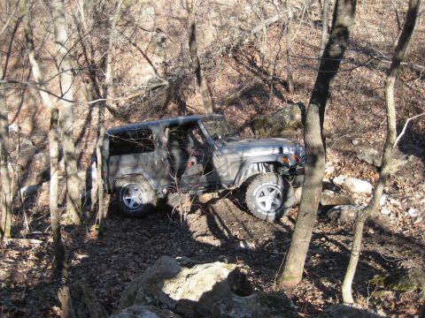 2005 Jeep Wrangler - A Jeep Wrangler is shown traversing a challenging, off-road path through a dense forest with rocky terrain.