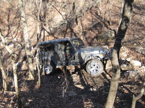 2005 Jeep Wrangler - A gray Jeep Wrangler navigates a steep, rocky, and wooded trail with its driver's door ajar.