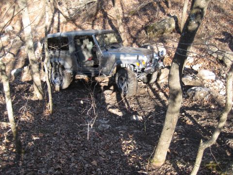 2005 Jeep Wrangler - A silver 2005 Jeep Wrangler is shown traversing a challenging off-road path through a wooded, rocky area.