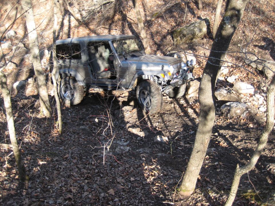 Silver 2005 Jeep Wrangler navigating a rocky, wooded trail