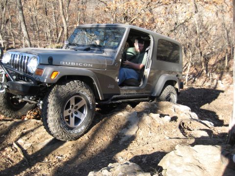 2005 Jeep Wrangler - A gray Jeep Wrangler Rubicon navigates a challenging rocky trail in a wooded area.