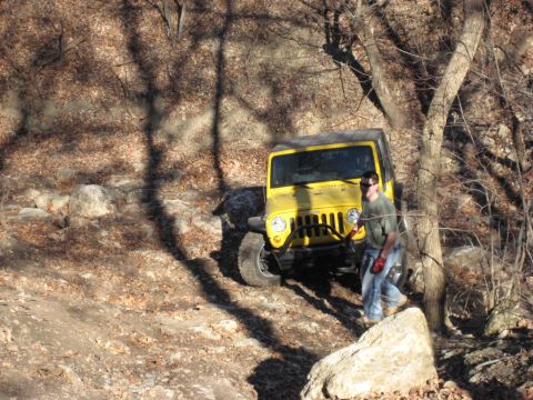 2005 Jeep Wrangler - A yellow Jeep Wrangler navigates a challenging off-road path through a wooded area.
