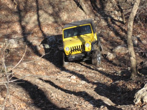 2005 Jeep Wrangler - A yellow Jeep Wrangler navigates a challenging off-road trail with steep inclines and loose rocks.