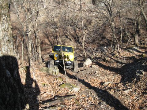 2005 Jeep Wrangler - A yellow Jeep Wrangler navigates a challenging, rocky off-road trail surrounded by bare trees.
