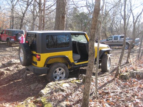 2005 Jeep Wrangler - A yellow Jeep Wrangler navigates a wooded, rocky terrain alongside other vehicles.
