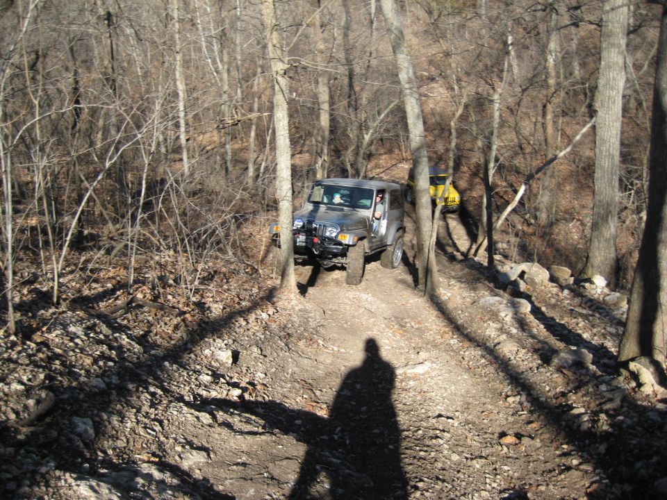 Silver 2005 Jeep Wrangler on a wooded trail, yellow Jeep behind it