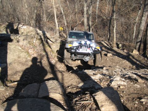 2005 Jeep Wrangler - A silver Jeep Wrangler navigates a challenging rocky terrain on a wooded trail.