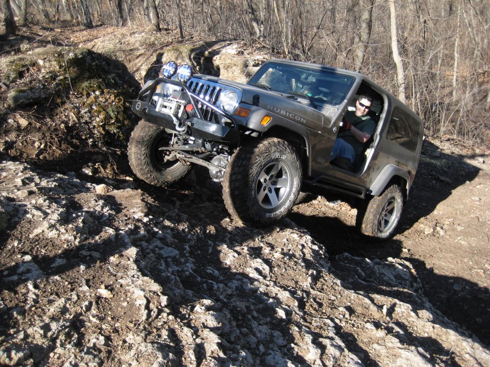Jeep Wrangler Rubicon climbing a rocky trail. Driver visible inside
