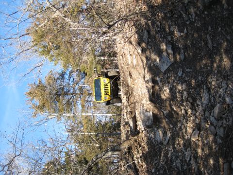 2005 Jeep Wrangler - A yellow Jeep Wrangler navigates a steep, rocky trail surrounded by trees under a clear blue sky.