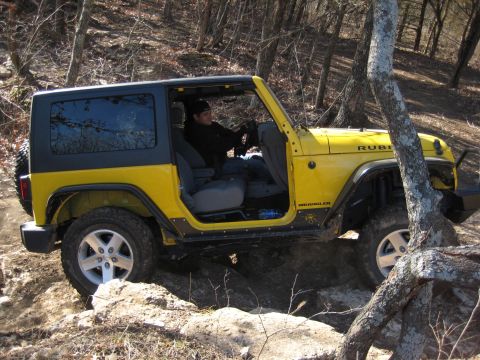 2005 Jeep Wrangler - Driver navigates a yellow 2005 Jeep Wrangler Rubicon over rough terrain on a wooded trail.