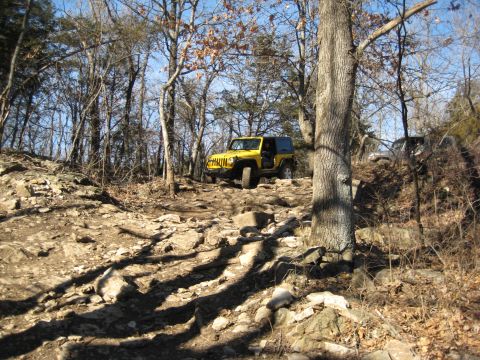 2005 Jeep Wrangler - A yellow Jeep Wrangler navigates a challenging, rocky off-road trail in a wooded area.