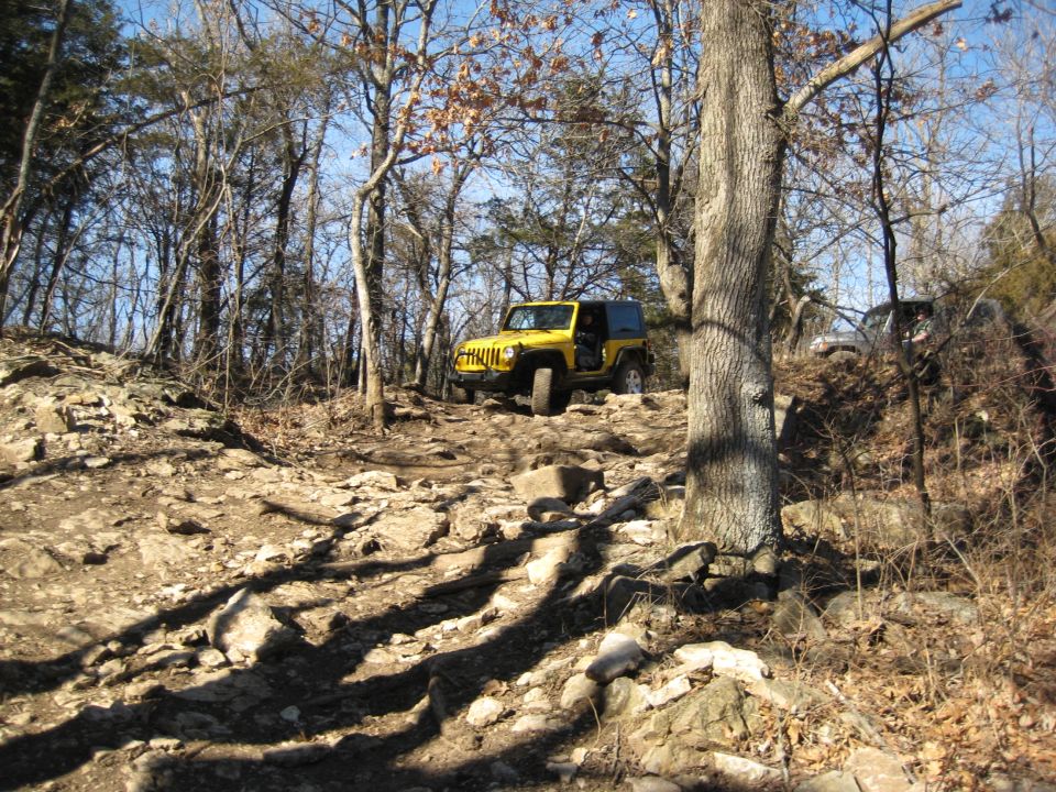 Yellow Jeep Wrangler climbing a rocky hill with another vehicle behind it
