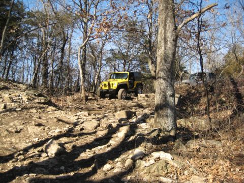 2005 Jeep Wrangler - A yellow Jeep Wrangler navigates a challenging, rocky off-road path in a wooded area.