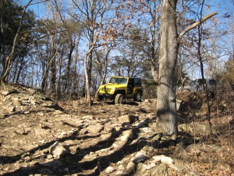 2005 Jeep Wrangler - A yellow 2005 Jeep Wrangler navigates a challenging rocky terrain, with another vehicle visible further up the trail.