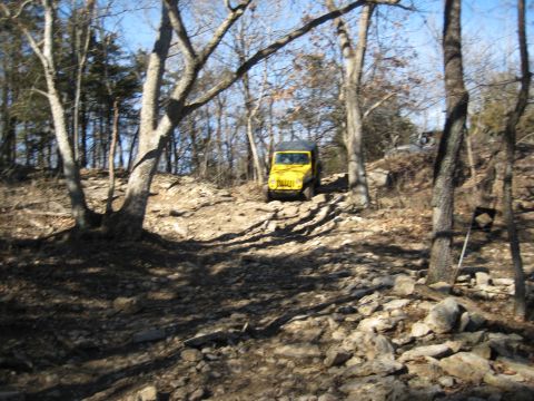 2005 Jeep Wrangler - A yellow Jeep Wrangler navigates a challenging, rocky incline in a wooded area.