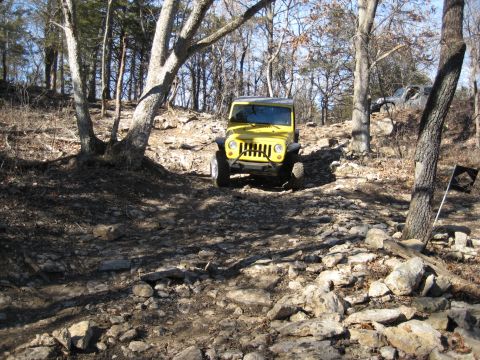 2005 Jeep Wrangler - A yellow Jeep Wrangler navigates a challenging, rocky off-road path through a wooded area.