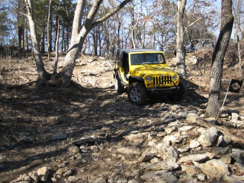 2005 Jeep Wrangler - A yellow Jeep Wrangler navigates a rocky off-road trail with another vehicle visible in the background.