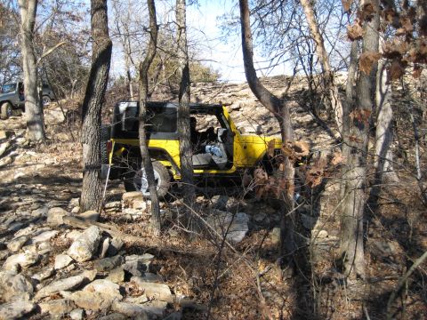 2005 Jeep Wrangler - Two Jeeps tackle a challenging, rocky off-road course surrounded by trees and sparse foliage.