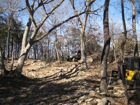 2005 Jeep Wrangler - Two Jeep Wranglers navigate a challenging rocky path through a dense forest on a clear day.