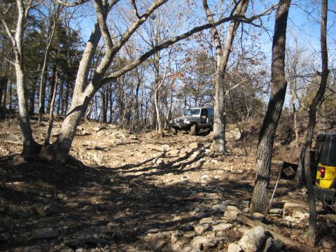 2005 Jeep Wrangler - A silver 2005 Jeep Wrangler navigates a rocky off-road trail, with a yellow Jeep partially visible on the right side of the frame.