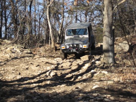 2005 Jeep Wrangler - A Jeep Wrangler navigates a challenging, rocky path through a wooded area on a sunny day.