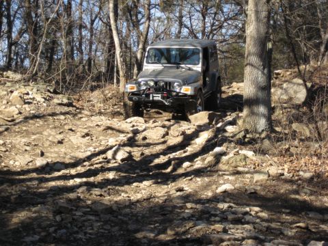 2005 Jeep Wrangler - A silver 2005 Jeep Wrangler navigates a challenging rocky terrain in a wooded area.