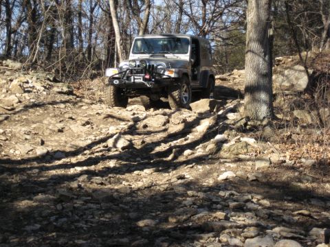 2005 Jeep Wrangler - A silver 2005 Jeep Wrangler navigates a challenging rocky path through a wooded area.