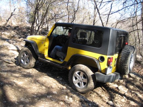 2005 Jeep Wrangler - A yellow Jeep Wrangler navigates a rough, wooded terrain with its doors removed.