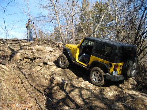 2005 Jeep Wrangler - A yellow Jeep Wrangler navigates a challenging rocky terrain on a sunny day.