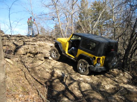 2005 Jeep Wrangler - A yellow Jeep Wrangler navigates a steep, rocky off-road trail with a person standing on the ridge above.