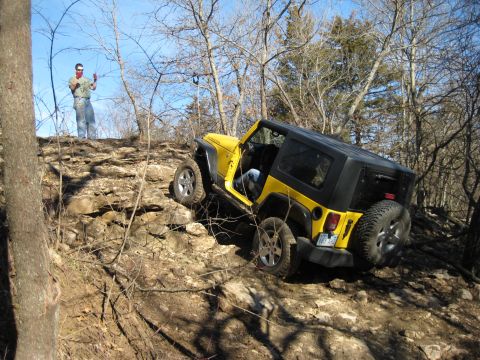 2005 Jeep Wrangler - Yellow Jeep Wrangler tackling a challenging rocky off-road course with a person observing from above.