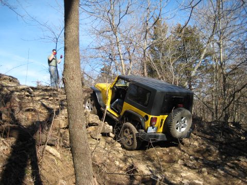2005 Jeep Wrangler - A yellow Jeep Wrangler is shown off-roading on a rocky trail, with a person observing from a higher elevation.