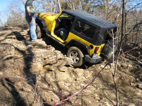 2005 Jeep Wrangler - A yellow Jeep Wrangler is shown off-roading on a rocky trail, demonstrating its capabilities on challenging terrain.