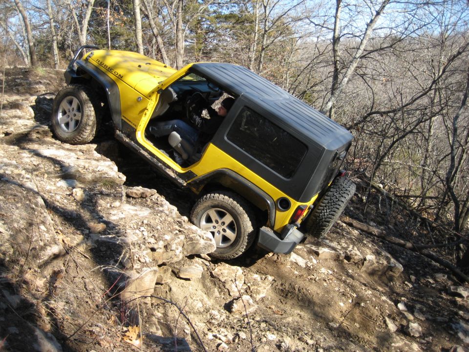 Yellow Jeep Wrangler with a black top driving over rocks on a trail. The word "Rubicon" is visible on the hood