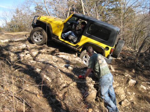 2005 Jeep Wrangler - A yellow 2005 Jeep Wrangler Rubicon is shown tackling a challenging rocky terrain, with a person assisting from the side.