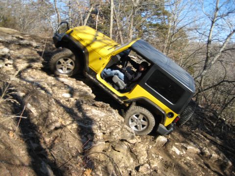 2005 Jeep Wrangler - A yellow Jeep Wrangler navigates a steep, rocky trail in a wooded area.