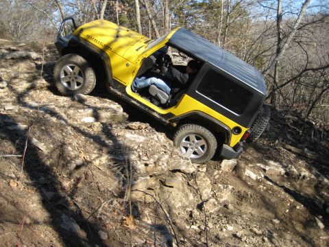 2005 Jeep Wrangler - A yellow 2005 Jeep Wrangler Rubicon navigates a challenging rocky trail, demonstrating its off-road capabilities.