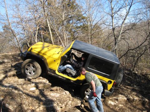 2005 Jeep Wrangler - A yellow Jeep Wrangler Rubicon is being driven over rocks with assistance from someone outside the vehicle.