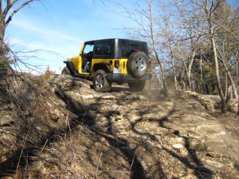 2005 Jeep Wrangler - A yellow Jeep Wrangler navigates a dusty, rocky trail through a wooded area.