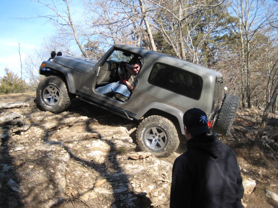 Gray 2005 Jeep Wrangler with a hardtop, driving off-road over large rocks. The driver is visible inside