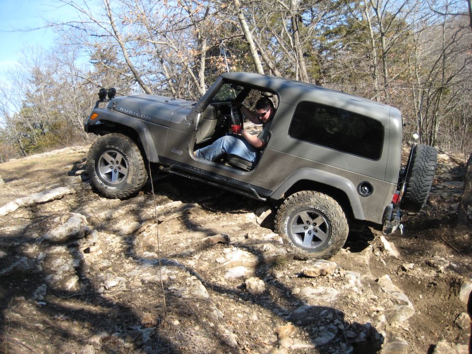 Gray Jeep Wrangler Rubicon driving over rocks on a trail. Driver is wearing jeans and a t-shirt