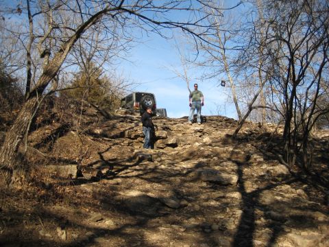 2005 Jeep Wrangler - Two people stand on a rocky incline next to a 2005 Jeep Wrangler, navigating off-road terrain.
