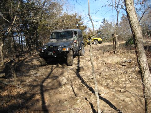 2005 Jeep Wrangler - Two SUVs navigating a rough, off-road trail through trees.