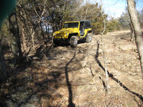 2005 Jeep Wrangler - Yellow Jeep Wrangler navigating a rough, rocky path through trees.