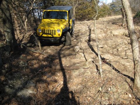 2005 Jeep Wrangler - A yellow Jeep Wrangler navigates a challenging rocky trail surrounded by trees and dry leaves.